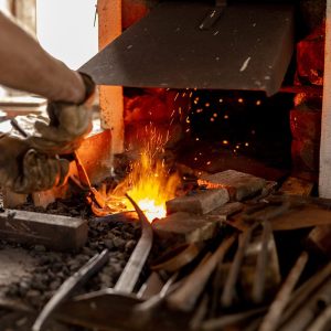 The blacksmith in production process of metal products, handmade in the forge. Craftsman heats metal in the fire. Metal industry, old profession